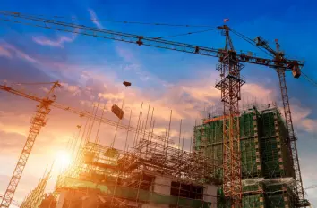 Construction cranes and building framework at sunset, representing commercial construction and jobsite applications.