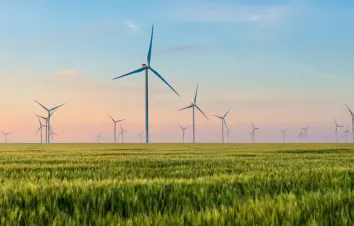 Wind turbines in a green field at sunset, representing renewable energy and wind power applications.