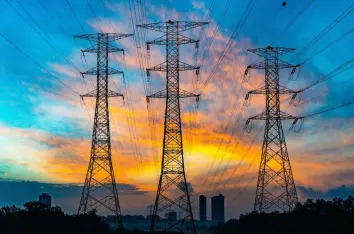 High-voltage electrical transmission towers and power lines against a sunset sky.